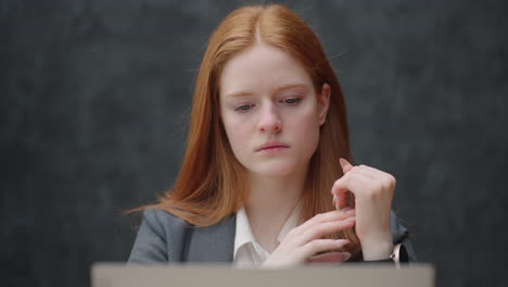 A-young-red-haired-business-woman-looks-thoughtfully-at-the-screen-and-brainstorms.-Watch-and-think-about-problems-looking-out-the-window.-Thoughtful-business-woman